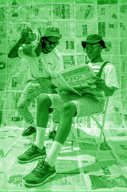 Female sitting reading a newspaper with male behind carrying karaoke