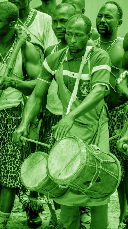 Man banging on two drums with men in background marching with him
