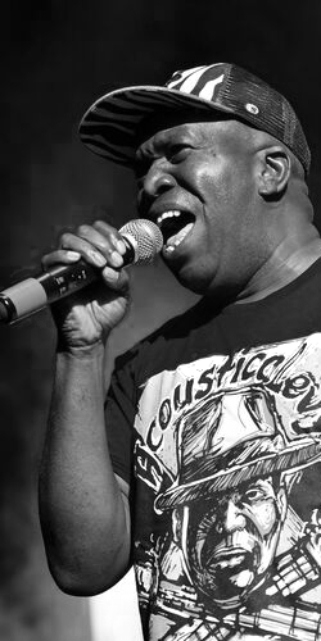 Male artist singing into a microphone wearing a hat.