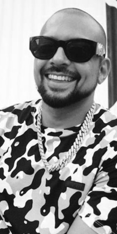 Male artist wearing sunglasses and chains smiling at camera